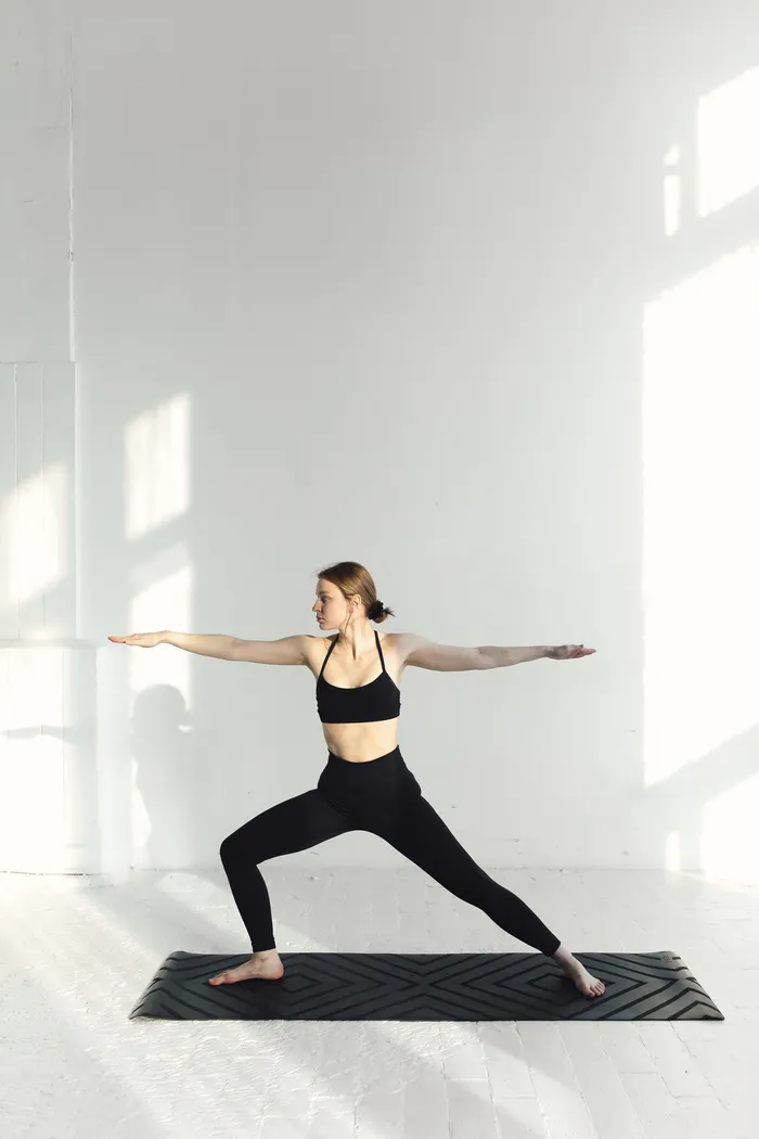 Mover holding a warrior two pose on a mat in a bright, minimal room